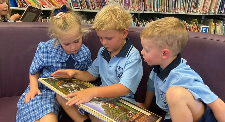 Three kinder students sitting on a lounge and reading together in the school library